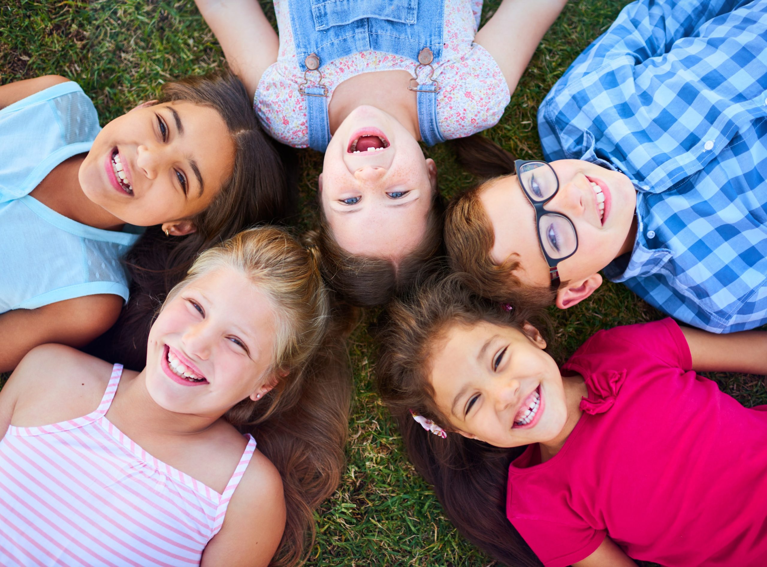 Kids laying down in a group smiling with crooked bottom teeth