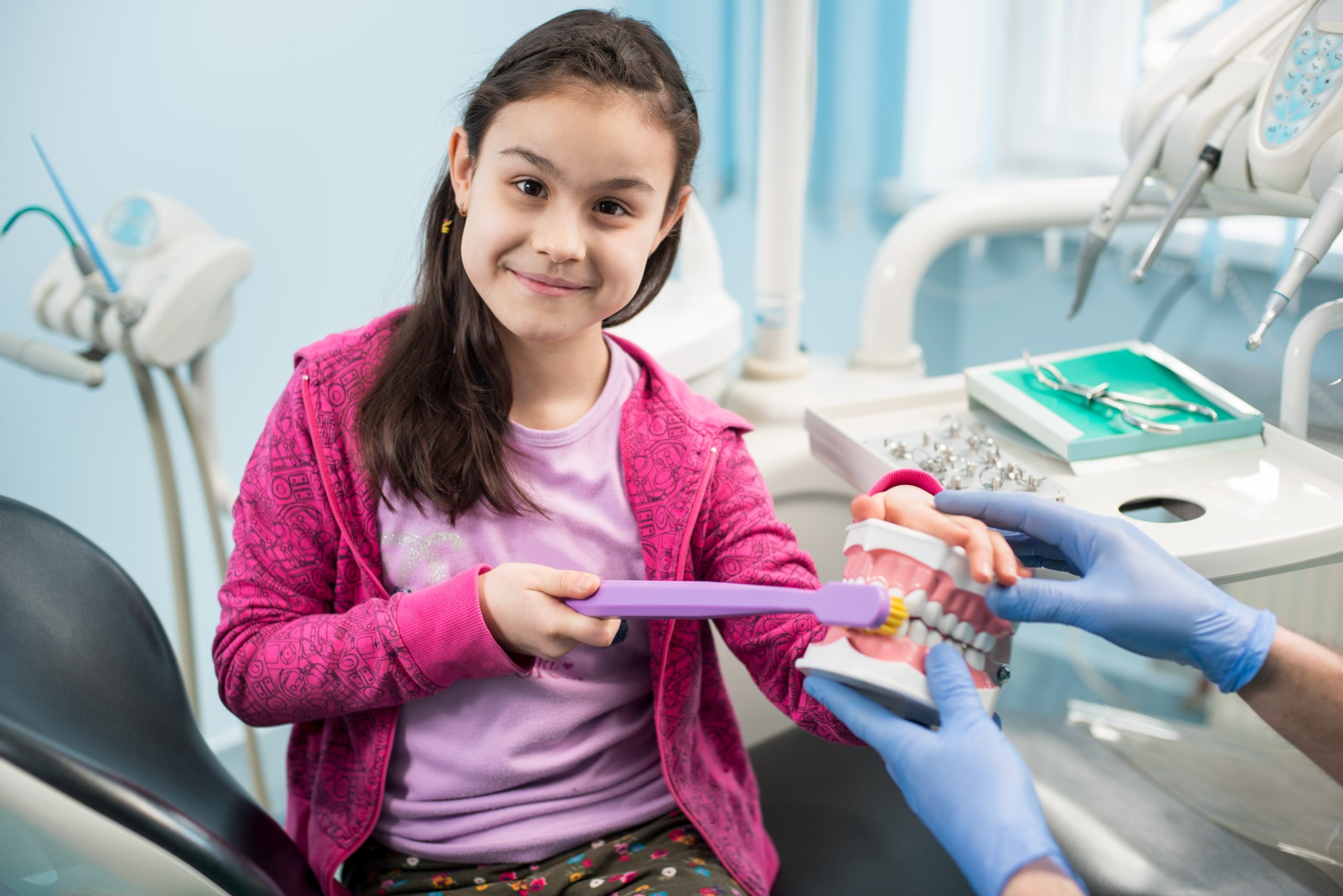 a child being shown a dental model and proper brushing technique to keep permanent teeth healthy