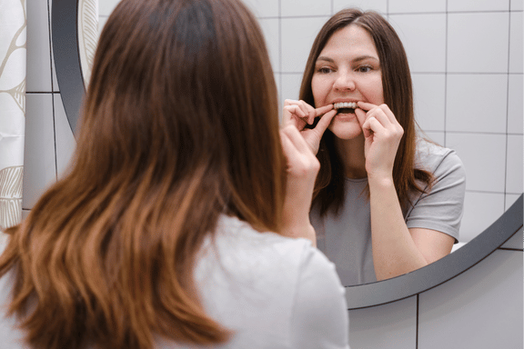 female adult inserts invisalign clear aligner on upper teeth looking in a mirror