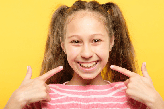 a young girl pointing to her permanent teeth that have all come in 