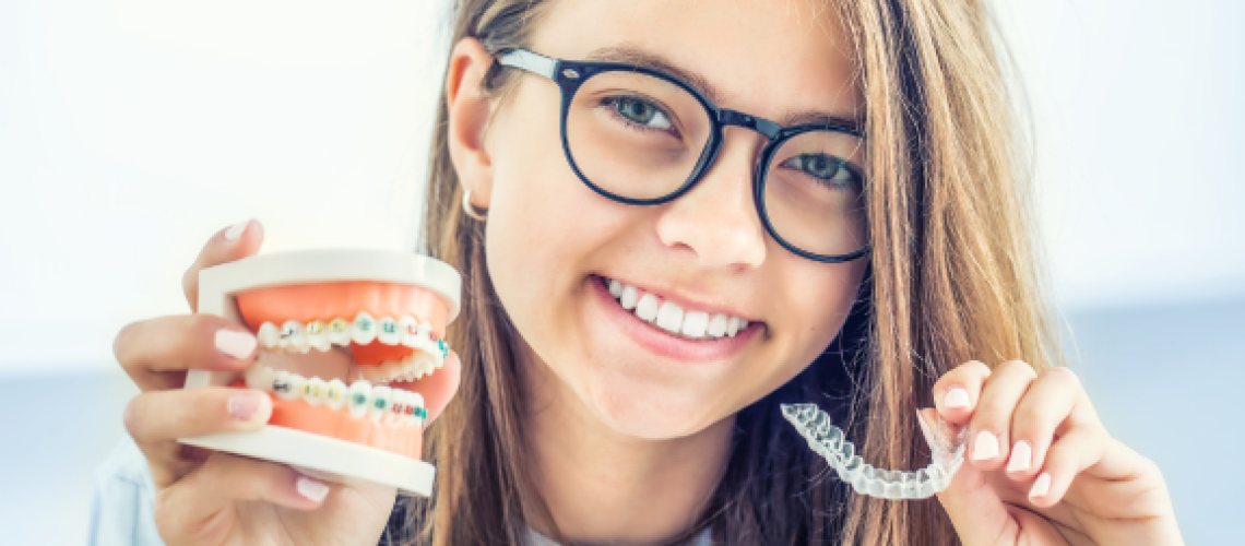 teen girl holding up a dental model with braces and a clear aligner